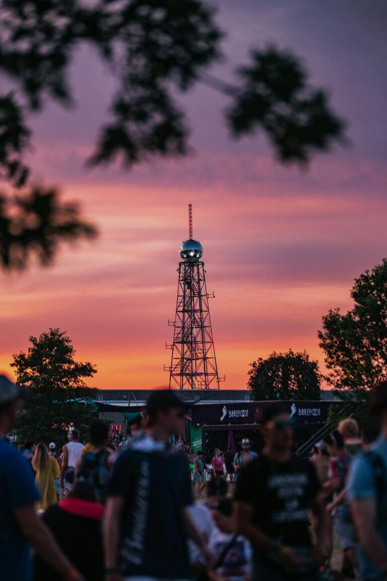 A lively outdoor festival scene at dusk with people gathered and a prominent tower in the background.