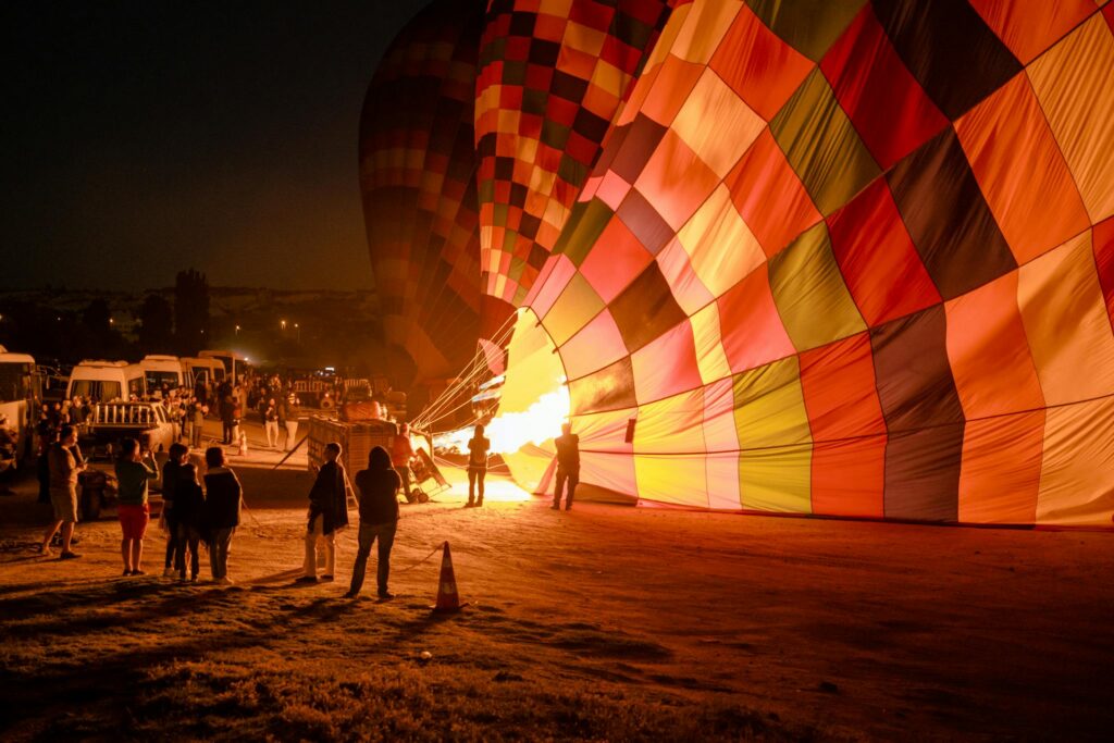 Colorful hot air balloon inflating at a nighttime festival with silhouetted spectators.